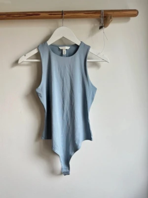 Body - Säljer en ljusblå ärmlös body från H&M med rund halsringning och tight passform. Toppen är tillverkad i mjuk bomull och har en enkel, stilren design som passar perfekt till jeans eller kjol.