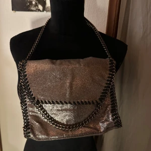 Glittrig silver axelväska med kedja - Säljer en glittrig silverfärgad axelväska med grov kedja som axelrem och snygga detaljer längs kanterna. Väskan har ett lock och magnetknäppning, perfekt storlek för det viktigaste. Materialet är syntet och har en metallic finish som verkligen sticker ut.