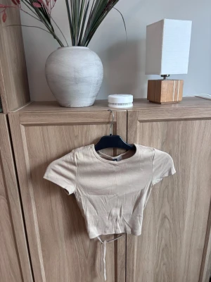 Beige topp - Säljer en beige croppad topp från H&M Divided i storlek XXS. Toppen har knyt detalj i ryggen där bak. Prislapp kvar