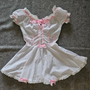 Vit handmade klänning från Malicious Designs - Vit handsydd klänning ''The Maja Dress'' från Malicious Designs. Mycket fint skick förutom lite nopprig på enstaka ställen, rosetterna har fransat sig lite och spetsen har gulnat pyttelite men inget som stör, se alla bilder. ''Onesize'' men jag uppskattar den passar en XS, den går dock att justera lite med snörningen i bak så kan eventuellt passa en XXS och liten S också. Jag köpte den för ca 2335 kr med frakt och importmoms inräknat.  Rökfritt hem men har katter.