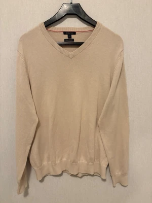 Beige v-ringad tröja från Batistini - Snygg beige v-ringad tröja från Batistini i storlek L. Tillverkad i mjuk pima bomull som känns skön mot huden. Tröjan har långa ärmar och ribbade muddar vid hals, ärmslut och nederkant. Perfekt att bära över en skjorta för en clean och stilren look.