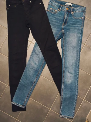 Skinny jeans KLASSISKA Molly fr GinaTricot MEN MED LÅG MIDJA - Två par jeansbyxor från Molly, ett par i klassiskt svart och ett par i ljusblå. Båda har skinny passform, fem fickor och dragkedja med knapp framtill. Materialet är stretchig bomull med jeanskänsla. Perfekt för dig som gillar tajta jeans med enkel stil. Observera att detta är Molly från Gina Tricot klassisk stil men med låg midja. Nyskick