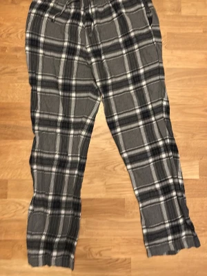 Grå-rutiga mjukisbyxor XL - Säljer ett par grå mjukisbyxor i storlek XL från C. Byxorna har ett rutigt mönster i svart, vitt och grått, samt dragsko i midjan för skön passform. Perfekta för chill dagar hemma eller när du vill vara extra bekväm.