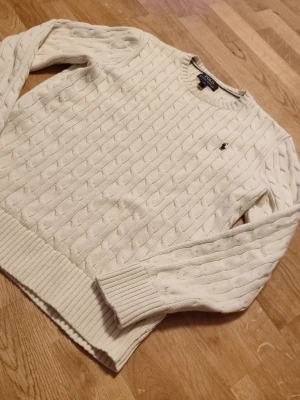 Beige kabelstickad tröja Polo Ralph Lauren - Säljer en beige kabelstickad tröja från Polo Ralph Lauren i storlek junior L. Tröjan har rund hals, ribbade muddar och det klassiska broderade Polo-logot på bröstet. Perfekt för dig som gillar stilrena och tidlösa plagg med snygg struktur. Tröjan passar dig som är mellan 160- 168cm
