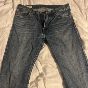 Levi's 501 blå jeans straight fit - Klassiska blå Levi's 501 jeans med rak passform och femficksdesign. Jeansen har den ikoniska läderpatchen bak i midjan och röd Levi's-tagg på bakfickan. Tillverkade i slitstarkt bomullsjeans med knappgylf och snyggt tvättad look.