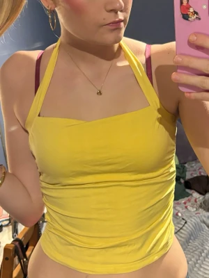 Gul halterneck linnetopp - Snygg gul halterneck topp med knytning i nacken. Toppen är croppad och har en enkel, stilren design som passar perfekt till sommaren. Gjord i mjukt bomullsmaterial som känns skönt mot huden. Perfekt att matcha med jeans eller kjol för en fräsch look.