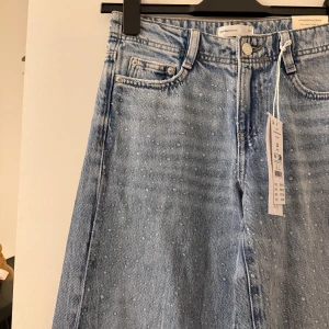 Low waist jeans  - Säljer ett par ljusblå jeans från Gina i modellen wide med pärldetaljer över hela framsidan. Jeansen  är low waist och helt nya då det var fel storlek för mig. 