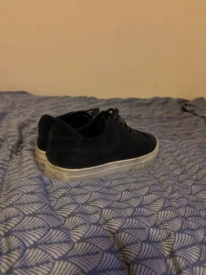 Svarta sneakers från Vagabond - Säljer ett par mörkblå sneakers från Vagabond i mocka med klassisk låg profil och vit sula. Skorna har snörning och en stilren design som passar till det mesta. Perfekta för dig som gillar enkel och clean stil. Skorna har används hyfsat länge och är ändå i gott skick! Hör av er vid någon fråga