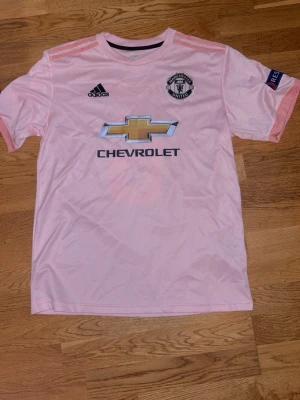 Man Utd tröja - Bilderna visar en rosa Manchester United-tröja med Pogba och nummer 6 på ryggen, samt Chevrolet-logga på framsidan. Ingen sko finns på bilderna.