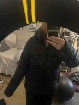 Svart pufferjacka med huva - Säljer en svart pufferjacka med huva och dragkedja framtill. Jackan har en quiltad look och är långärmad med en loose passform. Perfekt för kalla dagar när du vill vara både varm o chill. KNAPPT ANVÄND!!