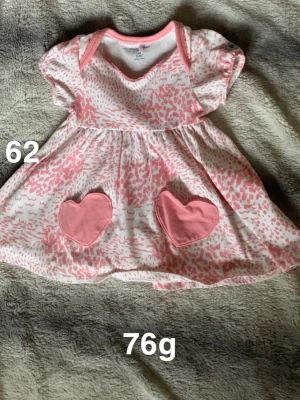 Söt rosa och vit klänning med hjärtan - Supergullig kort klänning från Polarn O. Pyret i storlek 62. Klänningen är vit med rosa prickigt mönster och har två hjärtformade fickor framtill. Kortärmad, perfekt för små barn.🌸 Fint använt skick. Storlek 62