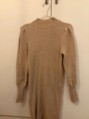 Only - Stickad klänning, figurnära när den sitter på, lite högre i kragen och puffärmar som slimmas ut mot handleden. Slutar i mitten av låret. 