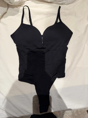 Svart body från H&M med vadderade kupor - Svart body från H&M i storlek M med vadderade kupor och justerbara axelband. Tillverkad av mjukt material med stretch för en bekväm passform. Perfekt att styla med jeans eller kjol för en snygg look.