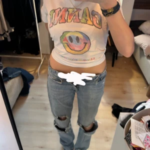 Blå ripped jeans från Zara, strl 34 - Säljer ett par blå jeans från Zara i storlek 34 med flera stora slitningar och hål på benen för en edgy look. Modellen är rak och midwaist, med klassisk femficksdesign och knappgylf. Perfekta för dig som gillar streetstyle och vill sticka ut.