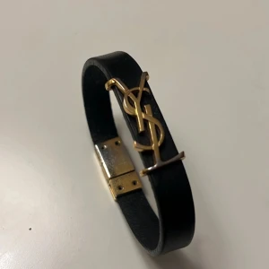 YSL armband  - Säljer nu mitt YSL armband som jag köpte på NK i Göteborg 2022 som inte kommer till användning. (Str: S = 16cm) Det har försvunnit lite av guld pläteringen på loggan och vid låset. Inget man tänker på du bär det. Box, dustbag till armbandet och kvitto följer med. Hör av dig om du är intresserad!