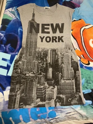 Grey New York Graphic Sleeveless Top – Rhinestone Details  - Stylish grey sleeveless top with a New York city skyline print and subtle rhinestone/stud details that add a cool street-style vibe. Soft and comfortable fabric, perfect for everyday wear or dressing up with jeans or a skirt.