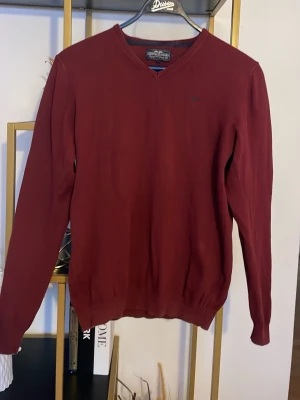 Vinröd v-ringad tröja från Hampton republic - Säljer en vinröd v-ringad tröja från Hampton republic. Tröjan har lång ärm och ribbade muddar vid ärmslut och nederkant. Materialet är mjuk bomull och passformen är normal. Perfekt för dig som gillar stilrena och enkla plagg.