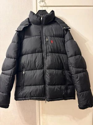 Svart pufferjacka från Polo Ralph Lauren - Svart pufferjacka från Polo Ralph Lauren  i stolek M. Den har legat nedvikt en stund därför ser den lite skrynklig ut endast använt några gånger. 