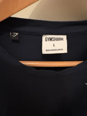 Mörkblå Gymshark t-shirt - Snygg mörkblå t-shirt från Gymshark med diskret logga på bröstet. Klassisk rund halsringning och korta ärmar. Perfekt för dig som gillar enkel och stilren design. Tillverkad i mjukt material som känns skönt mot huden.