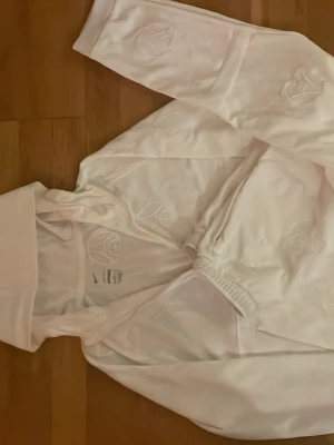 Vit PSG x Nike träningströja - Säljer en vit träningströja från Nike i samarbete med PSG. Tröjan har halv dragkedja, broderade PSG-loggor och Nike-märke på bröstet. Tillverkad i mjukt funktionsmaterial, perfekt för träning eller sportiga outfits.