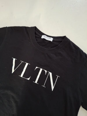 Svart VLTN t-shirt från Valentino - Svart t-shirt från Valentino med VLTN-tryck i vitt på bröstet. Klassisk rund hals och korta ärmar. Tillverkad i mjuk bomull, perfekt för en clean och stilren look. Made in Italy för extra lyxig känsla.