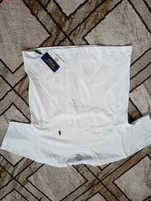 Vit t-shirt från Polo Ralph Lauren - Klassisk vit t-shirt från Polo Ralph Lauren med rund hals och den ikoniska mörkblå broderade loggan på bröstet. Tillverkad i mjuk bomull och har en normal passform. Perfekt basplagg för en clean och stilren look.