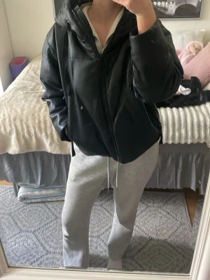 Svart oversized skinnjacka med huva - Säljer en svart oversized skinnjacka med dragkedja och stor huva. Jackan har en avslappnad passform och värmer förvånansvärt bra i kyliga temperaturer. Kunde ha den i mitten av februari, endast med en t shirt under och blev supervarm vid lugna cykelturer. Är ickemed på bilden men har litet slitagevid höger nacke. 