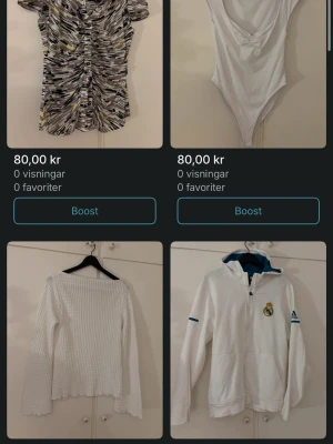 Säljer på Vinted vackra toppar  - Paket med fyra toppar: en mönstrad kortärmad blus i svart, vit och gul, en vit ärmlös bodysuit med djup v-ringning, en vit långärmad ribbad topp samt en vit långärmad sporttröja med dragkedja och Real Madrid-logga.