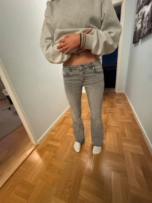 Grå bootcut jeans med låg midja - Säljer ett par grå bootcut jeans med låg midja och klassiska fem fickor. Jeansen har en lätt utsvängd passform nertill och synliga sömmar. Perfekta för en avslappnad och trendig look.