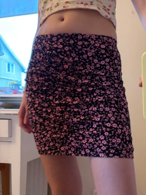 Svart minikjol med rosa blommor H&M - Säljer en svart kortkjol med rosa blommigt mönster. Kjolen har en åtsittande passform och rynkade detaljer framtill och baktill som ger en snygg effekt. ALDRIG ANVÄND!!! Väldigt skönt material🥰 bara att skriva om du undrar nåt eller vill ha mått💕💕