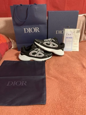 Dior B30 svarta och vita sneakers - Säljer ett par Dior B30 sneakers i svart och vitt med stora CD-loggor på sidorna. Skorna har en chunky vit sula och ovandel i kalvskinn och textil. Snygg design med kontrasterande detaljer och klassisk Dior-stil. Levereras med originalkartong, dustbag och påse.