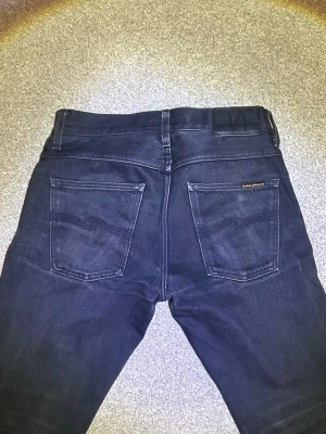 Nudie Jeans - Snygga svarta jeans från Nudie Jeans. Jeansen har diskreta sömmar och en liten logotyp på ena bakfickan. Perfekta för en stilren och avslappnad look.