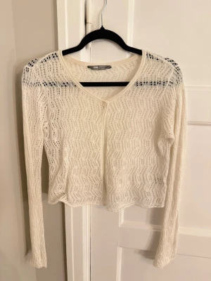 Vit virkad croppad topp cover up - Säljer en Vit virkad croppad topp cover up lång ärm och v-ringning. Tröjan har ett genombrutet, zigzag-mönster som ger en luftig och trendig look. Perfekt på stranden eller över linne som luftig kofta. Egentligen i kids storlek men passar även s-xxs beroende på passform 