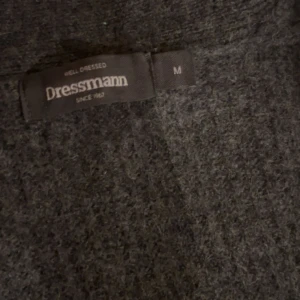 Mörkgrå kofta från Dressmann - Mysig mörkgrå kofta från Dressmann med sjalkrage och knäppning framtill. Koftan har två framfickor och är stickad i ett mjukt material, perfekt för lager-på-lager-stil.