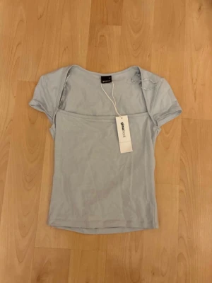 Ljusblå topp från Ginatricot - Supersöt ljusblå topp från Ginatricot med korta ärmar och figurnära passform. Tröjan är helt ny med prislappen kvar. Säljer då jag fått dubbletter. Tröjan är i storlek XS.