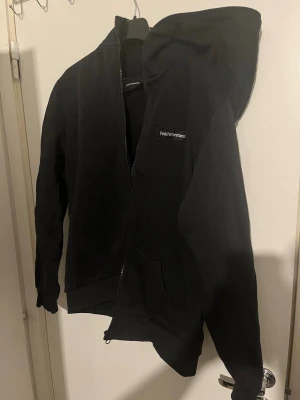 Svart Peak Performance hoodie - Snygg svart hoodie från Peak Performance med dragkedja och huva. Klassisk logga på bröstet och två fickor framtill. Tillverkad i mjukt och bekvämt material som passar perfekt till en avslappnad stil. Passar storlek L och M