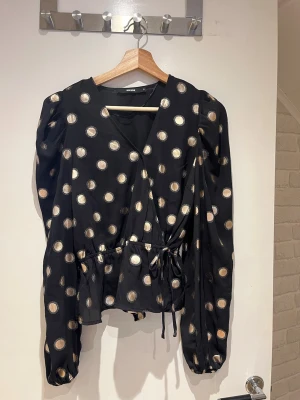 Svart omlottblus från BikBok - Snygg svart omlottblus från Bik Bok med guldiga prickar. Blusen har långa puffärmar, knytband i midjan och v-ringning. 