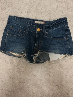 Levi's jeansshorts med fransig kant - Snygga blå jeansshorts från Levi's modell 506 Skinny. Klassisk femficksdesign, låg midja och rå fransig kant nedtill. Tillverkade i 99% bomull och 1% spandex för en skön passform. Perfekta för sommaren!