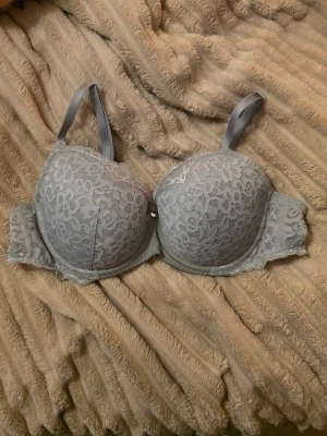 Ljusgrå spets-bh med blommönster - Snygg ljusgrå bh med vadderade kupor och vackert blommigt spetsmönster. Axelbanden är justerbara och bh:n har en liten dekorativ rosett framtill. Materialet är mjuk spets och tyg, vilket ger en feminin och elegant look. Använd max 3 ggr