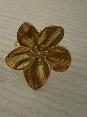 Två guldfärgade ringar med unik design - Säljer två snygga guldfärgade ringar. Den ena har en stor blomformad design med fina detaljerade blad, medan den andra har en organisk, skulptural yta som ger en cool och modern känsla. Båda ringarna är i metall och passar perfekt för dig som gillar statement-smycken.