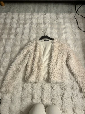 Vit teddyjacka från Gina Tricot - Supermjuk och fluffig vit teddyjacka från Gina Tricot. Jackan har öppen front utan knäppning och är helfodrad. Perfekt för att ge din outfit en mysig och trendig touch. Materialet är fuskpäls som känns riktigt lyxigt och skönt.