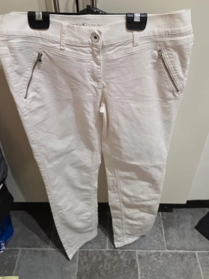 Vita super skinny jeans från Taifun - Säljer ett par vita super skinny jeans från Taifun med dragkedjor vid fickorna och klassisk femficksmodell. Jeansen har bälteshällor och knappgylf. Perfekta för dig som gillar en tajt passform och stilren look.