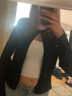 Vit croppad tubtopp med vågig kant - Vit, croppad tubtopp med vågig kant upptill. Toppen är ärmlös och har en enkel, stilren design som passar perfekt till jeans eller kjol. Snygg att bära under en öppen jacka eller kofta.