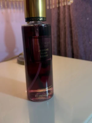 Victoria's Secret Jasmine Ruby Berry mist - En snygg doftmist från Victoria's Secret i doften Jasmine Ruby Berry. Flaskan är cylinderformad, genomskinlig med mörkröd vätska och har en guldfärgad kork. Rymmer 250 ml och har en lyxig look som passar perfekt i badrumshyllan.