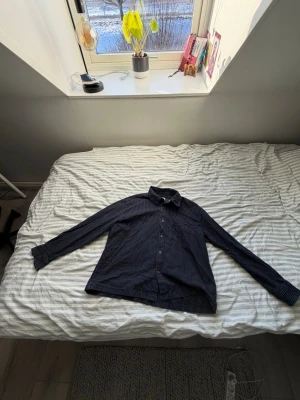 Svart randig skjorta med knappar - Svart skjorta med tunna vita/gröna  och klassisk krage. Skjortan har långa ärmar och knäppning framtill. Perfekt för en stilren och avslappnad look. Använd men jätte bra skick! 