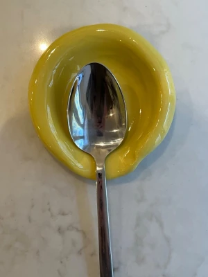 Gul keramik skedhållare - En handgjord skedhållare i keramik med blank gul glasyr i bubbelfat design. Formen är rundad med en liten urgröpning för att passa en sked, perfekt att ha bredvid spisen för att lägga av köksredskap. Färgen är klargul och ytan är glansig.