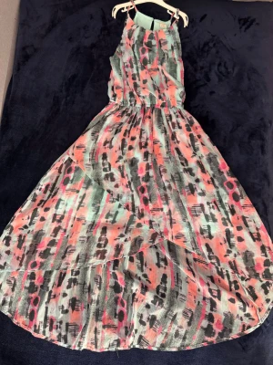 Långklänning med mönster - Säljer en långklänning med färgstarkt abstrakt mönster i rosa, svart, grått och mintgrönt. Storlek 158 i barnstorlek. Klänningen har ärmlös design och resår i midjan för en snygg passform. Perfekt för dig som gillar färg. 