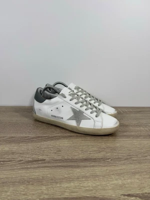 Golden Goose sneakers vit och grå  - Golden Goose sneakers i vitt med grå stjärna och bak inte andvända och i buy skick . Kvitto fins !