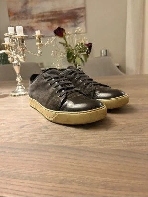 Svarta Lanvin sneakers i läder och mocka - Snygga svarta sneakers från Lanvin med ovandel i mocka och tåparti i blankt läder. Skorna har beige sula och klassisk låg profil med svarta skosnören. Perfekta för dig som gillar stilrena och exklusiva sneakers.