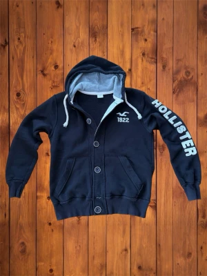 Vintage Hollister hoodie (sällsynt) - Säljer denna vintage sällsyna och asfeta hoodien/cardigan från Hollister. Riktigt fet och den Säljer denna vintage sällsyna och asfeta hoodien/cardigan från Abercrombie&Fitch. Riktigt fet och den är i väldigt bra skick och har en riktigt fet logga på armen. Storlek är  XXL vilket den verkligen inte passar som, passar som M se måtten nedan B=67cm A=57cm